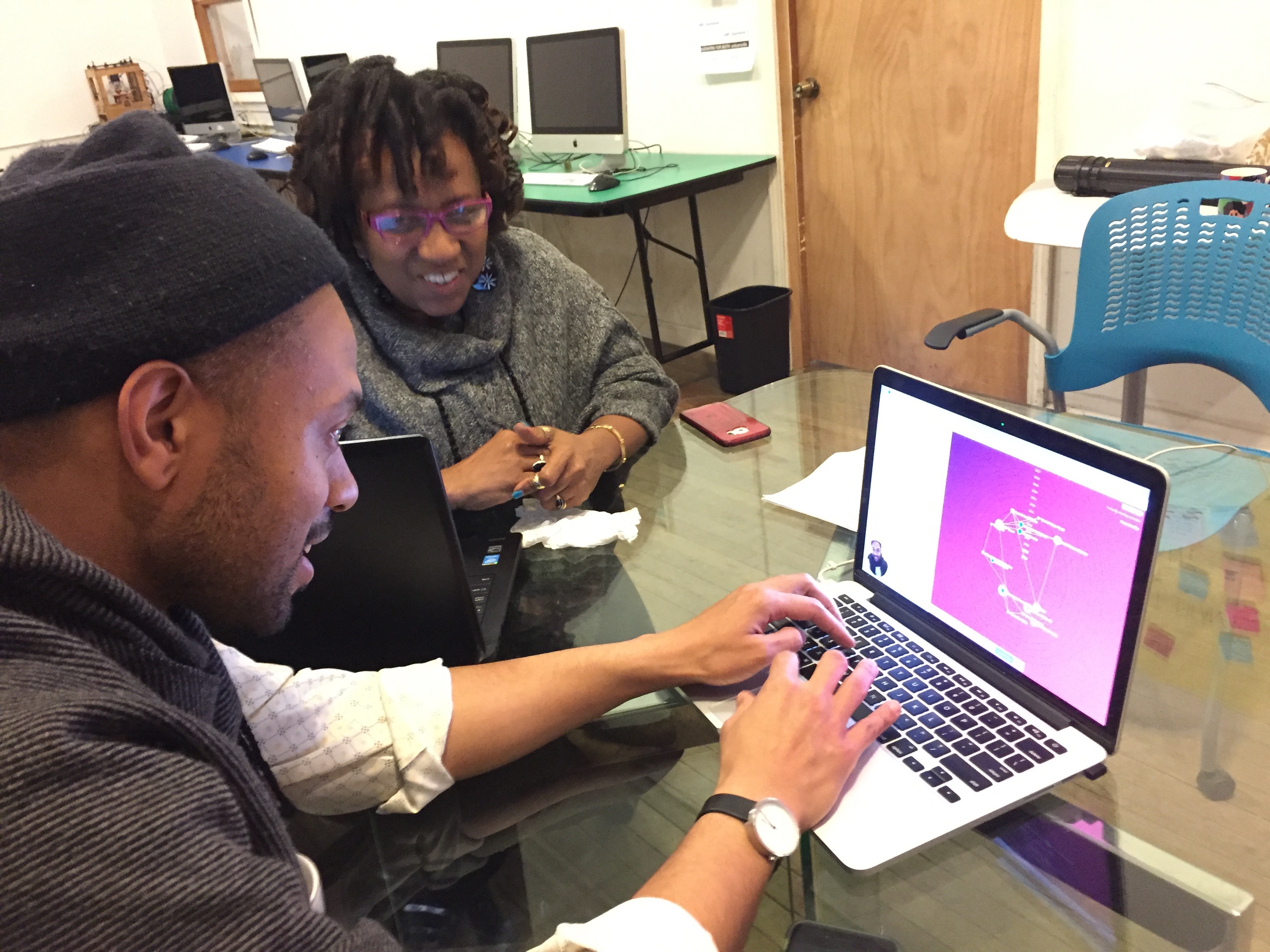 Two people sit in front of a laptop, which has the Ripple Mapping Tool open in a browser window. The person in the foreground uses the tool by typing on a keyboard while the other person watches.