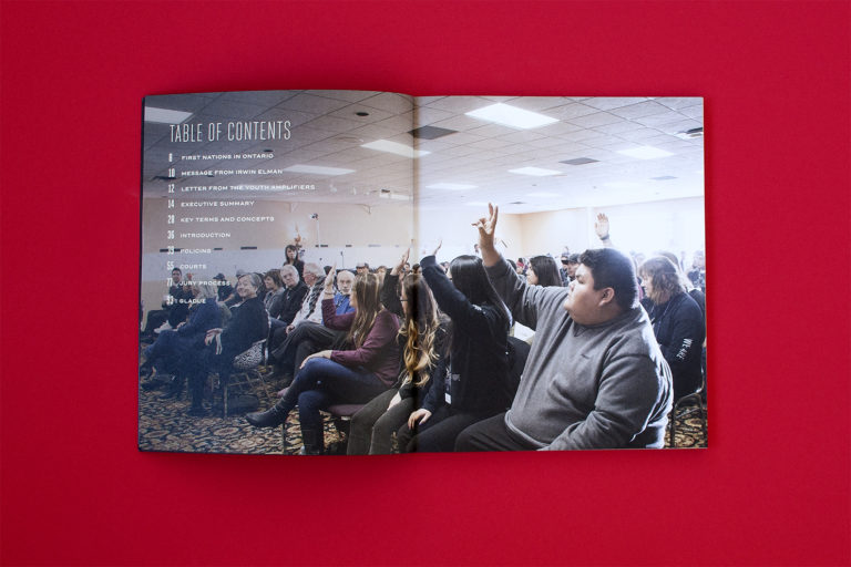 A full spread of the Table of Contents, featuring a full bleed image of a room full of people raising their hands.