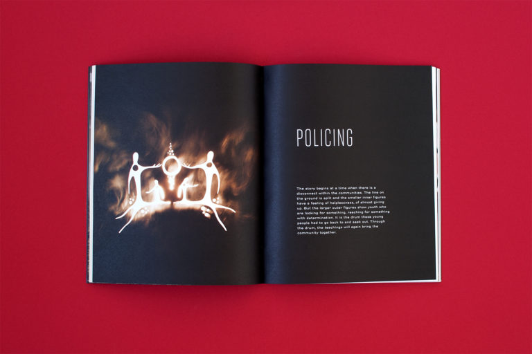 A full spread: The page on the right is an image of the backlit stencil illustration of stylized figures holding a drum. The page on the right is titled Policing