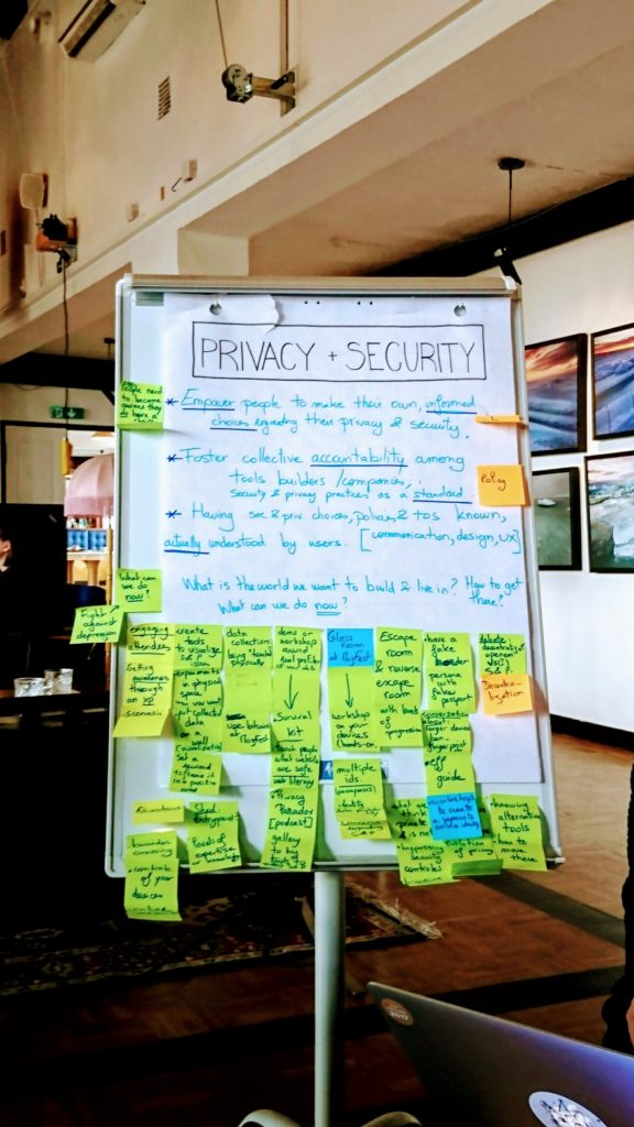 A photograph of a newsprint chart. The title reads ‘PRIVACY + SECURITY’, it is written in black and is outlined by a rectangle. Points below are written in a bright light blue text with, the keywords underlined in dark blue. There are a few post-its at the top of the chart paper and numerous post-its stuck to the bottom