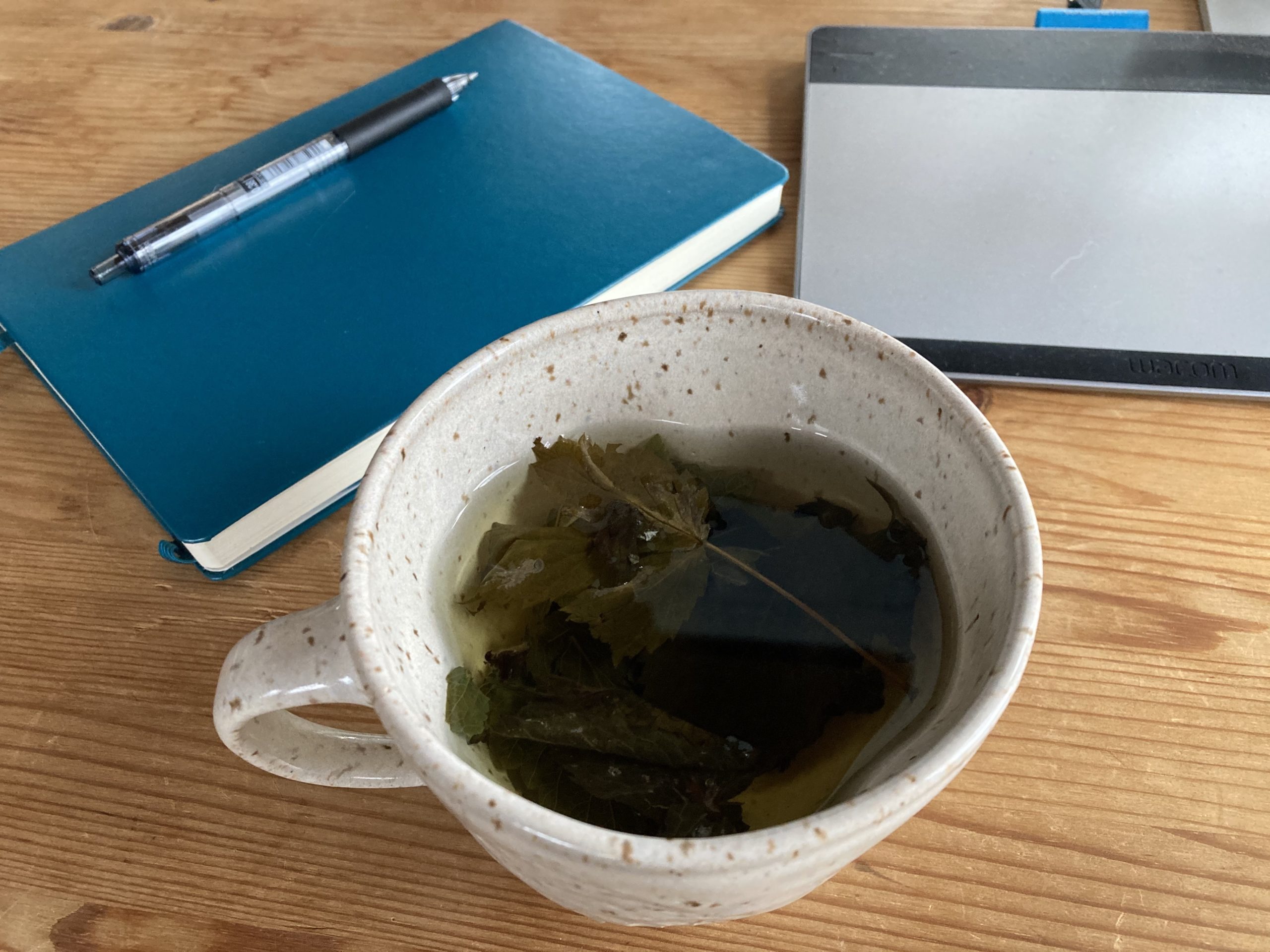 A speckled brown and cream colored ceramic cup with tea and tea leaves inside.