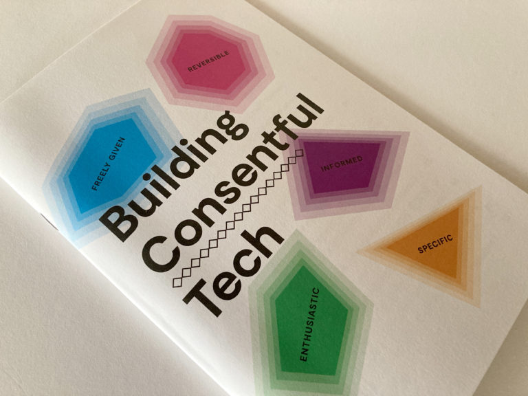 A photograph of the Building Consentful Tech zine on a table. The title is surrounded by gem shapes of different colors, with the words "Freely Given, Reversible, Informed, Enthusiastic, and Specific" inside of them.