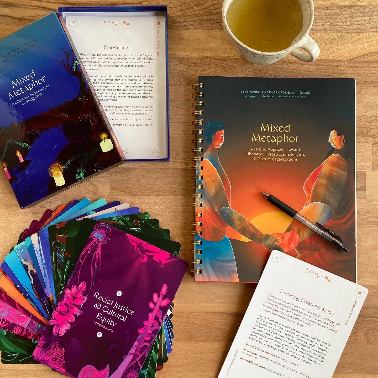An image of Mixed Metaphor booklet and card deck splayed out on a desk with a mug of tea